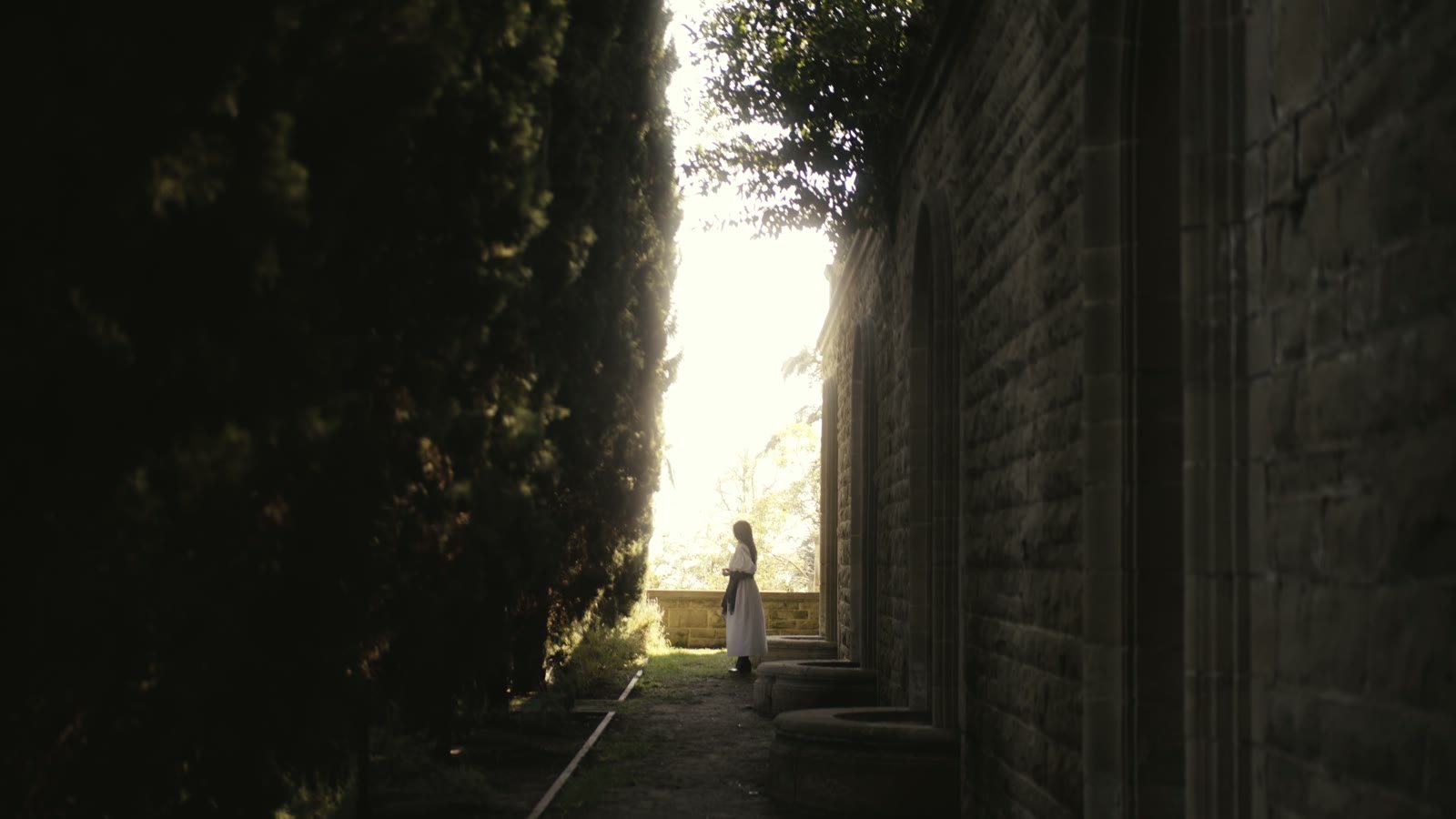 A figure in white on a garden path, from the Dracula's Speakeasy trailer.